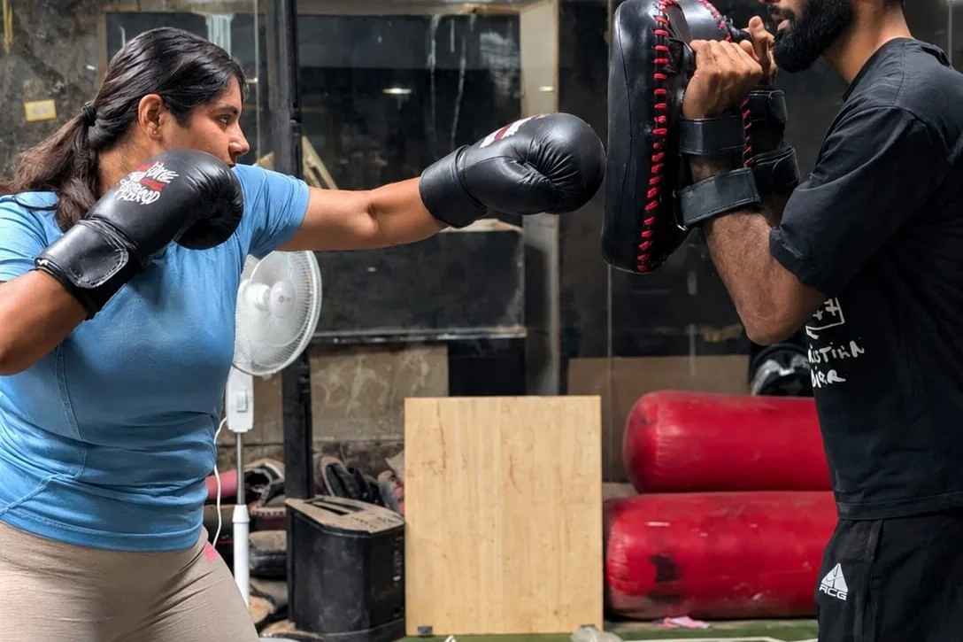 A woman throwing a jab-cross combination into focus mitts held by Coach Aditya at Redcrown MMA